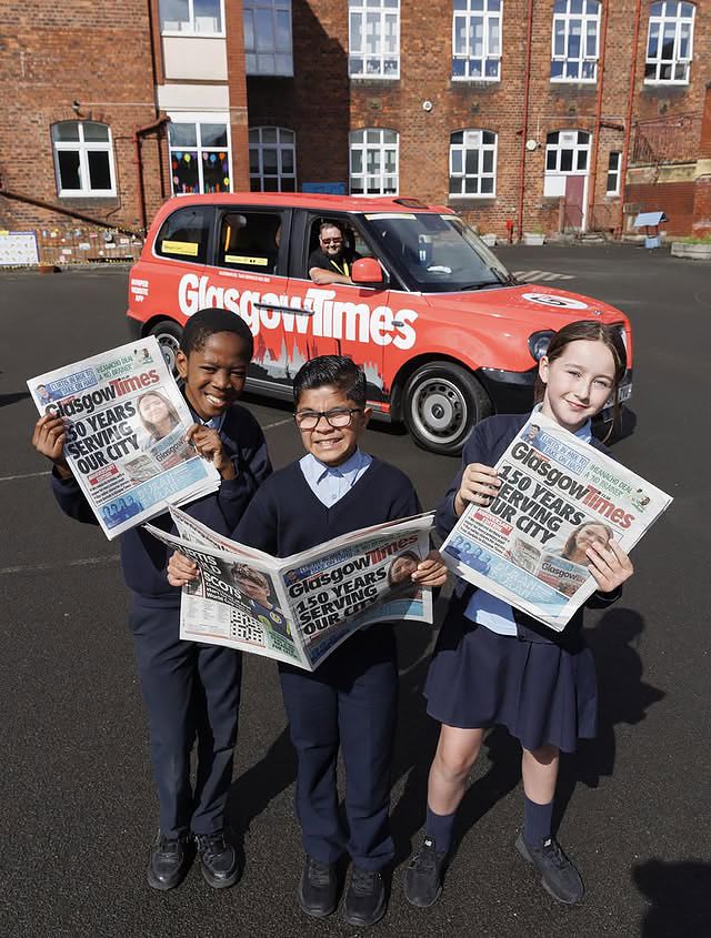 Pupils with the paper beside the wrapped Glasgow Times taxi